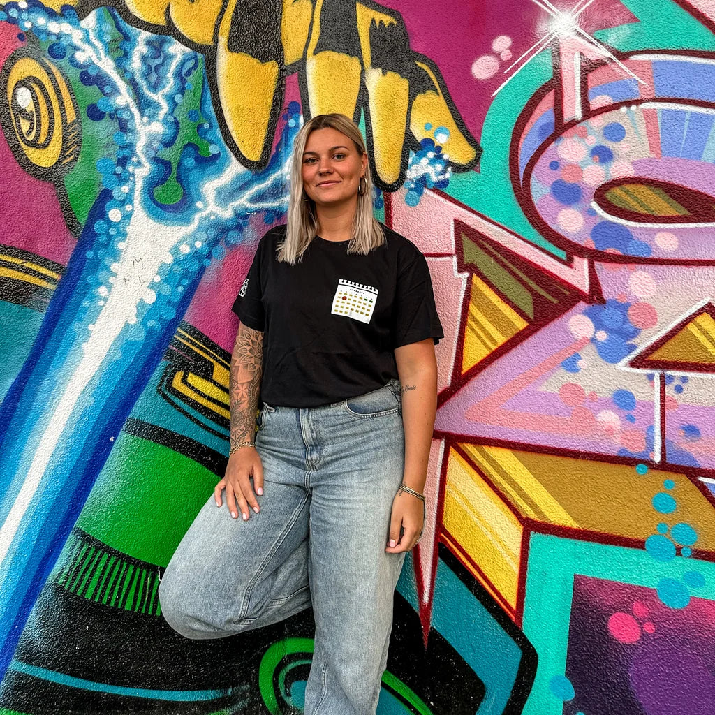 Zwart T-shirt met een kalender print van dinsdagdip op borst en logo van SNIVV op de mouw. Leuke en grappige kleding voor festivals voor dames